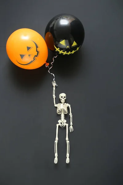 Skeleton with Halloween balloons on dark background