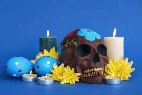 Painted skull for Mexico\'s Day of the Dead (El Dia de Muertos), flowers and burning candles on blue background