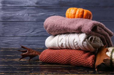 Çocuk süveteri yığını ve koyu ahşap arka planda sonbahar dekoru.