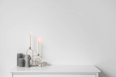 Beyaz duvarın yanındaki çekmecelerde yanan mumlar ve şık dekorlarla dolu bir tutucu.