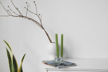 Mumlar, dergiler ve vazolar. Beyaz duvarın yanındaki çekmecelerde ağaç dalları var.