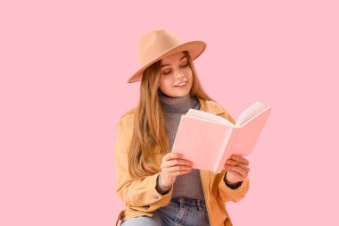 Pembe arka plan üzerine kitap okuyan genç bir kadın.