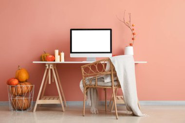 Pembe duvarın yanında bilgisayar, mum ve balkabağı olan işyeri