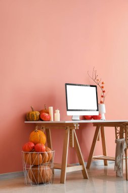 Pembe duvarın yanında bilgisayar, mum ve balkabağı olan işyeri