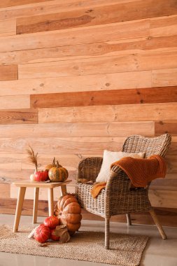 Kabaklı masa, vazo, dökülen yapraklar ve tahta duvarın yanındaki koltuk.