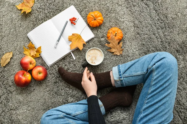 Young woman with cup of pumpkin coffee, opened notebook and autumn decor on plaid