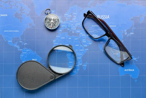 Magnifier, compass and eyeglasses on world map