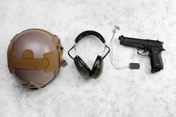 Military helmet, headphones, gun and tag on light background