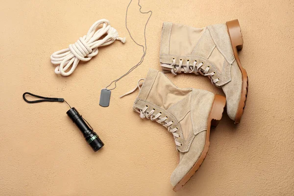 Military shoes, rope, flashlight and tag on color background