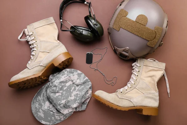 Military shoes, cap, helmet, headphones and tag on color background