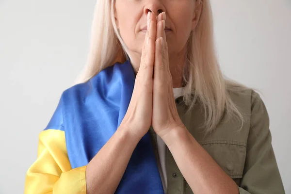 Mature woman with flag of Ukraine praying on light background, closeup