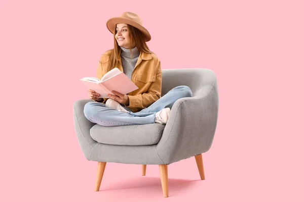 Kitabı Olan Genç Bir Kadın Pembe Arka Planda Koltukta Oturuyor — Stok fotoğraf