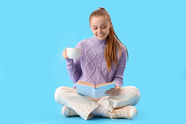 Mavi Arka Planda Sıcak Kakao Okuyan Genç Bir Kadın — Stok fotoğraf