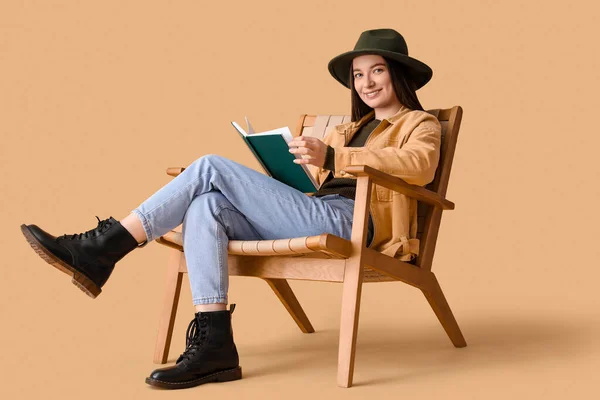 Νεαρή Γυναίκα Ανάγνωση Βιβλίο Στην Πολυθρόνα Μπεζ Φόντο — Φωτογραφία Αρχείου