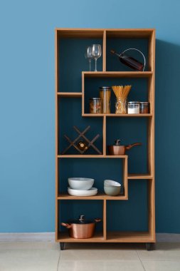 Mavi duvarın yanında yemek ve yemek takımı olan ahşap raf ünitesi.