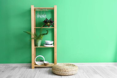 Ahşap raf ünitesi, yemek takımları, şarap şişeleri ve yeşil duvarın yanındaki bitki örtüsü.