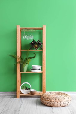Ahşap raf ünitesi, yemek takımları, şarap şişeleri ve yeşil duvarın yanındaki bitki örtüsü.