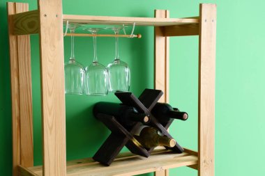 Ahşap raf ünitesi, yeşil duvarın yanında bardaklar ve şarap şişeleri.