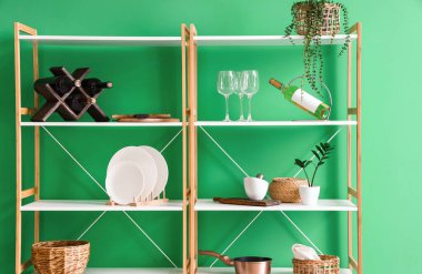 Mutfak gereçleri, ev bitkileri ve yeşil duvarın yanındaki içeceklerle raf ünitesi.