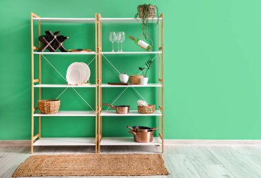 Mutfak gereçleri, ev bitkileri ve yeşil duvarın yanındaki içeceklerle raf ünitesi.