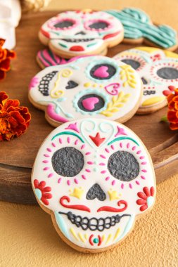 Kafatası şeklinde kurabiyeler ve bej arka planda çiçekler olan tahta. El Dia de Muertos