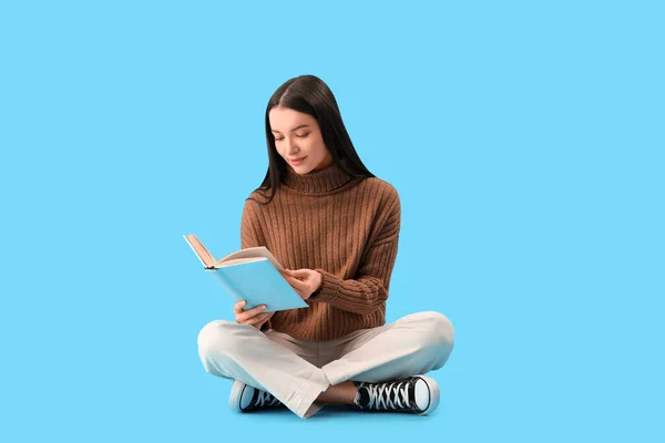 若いです女性でブラウンセーター読書本上の青の背景 — ストック写真