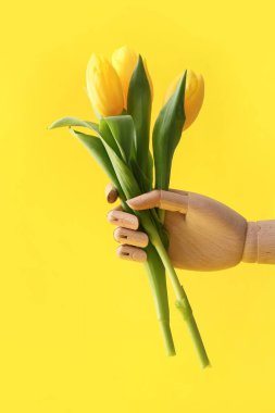 Sarı arka planda lale çiçekleri olan tahta bir el.