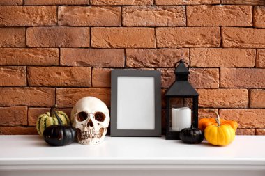 Cadılar Bayramı balkabaklarıyla boş çerçeve, şömine rafında fener ve kafatası tuğla duvarın yanında.