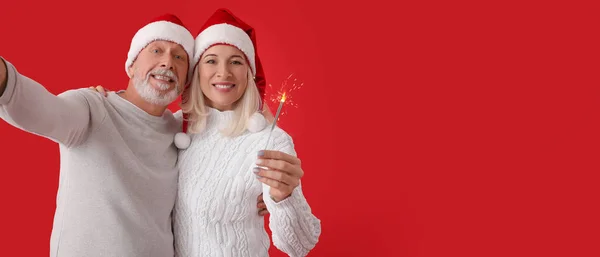Happy Mature Couple Santa Hats Sparkler Taking Selfie Red Background — Stock Photo, Image