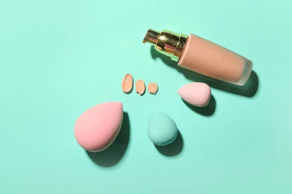 Bottle of makeup foundation and sponges on color background