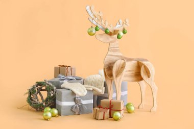 Noel topları, eldivenleri, şapkası ve bej arkaplanda hediyeleri olan tahta ren geyiği.