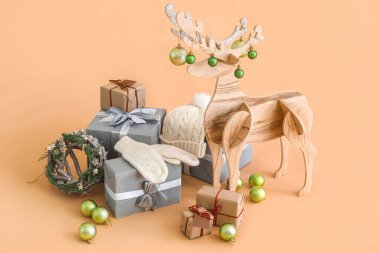 Noel topları, eldivenleri, şapkası ve bej arkaplanda hediyeleri olan tahta ren geyiği.