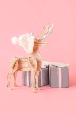 Pembe arka planda şapkalı, eldivenli ve Noel hediyeli tahta ren geyiği