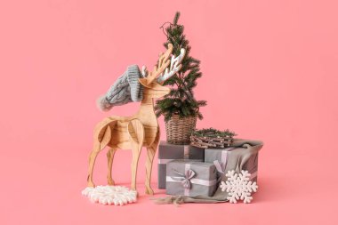 Şapkalı tahta ren geyiği, Noel ağacı ve pembe arka planda hediyeler.