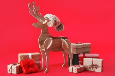 Noel Baba şapkalı tahta ren geyiği ve kırmızı arka planda Noel hediyeleri.