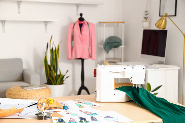 Workplace of fashion designer with sewing machine, cloth and sketches in studio