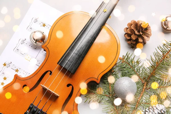 Violin with Christmas decor and music note sheets on light background