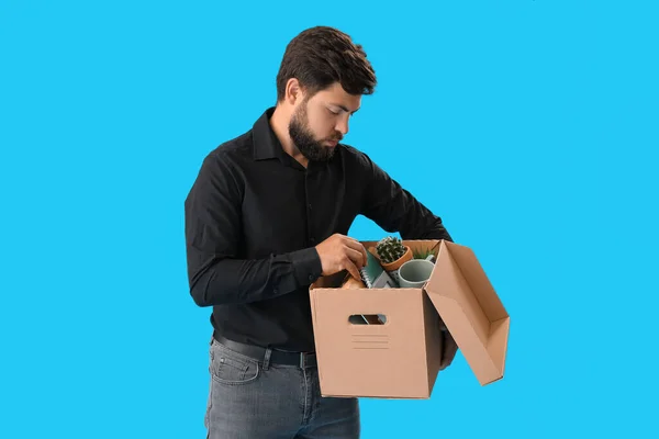 Fired young man holding box with his office stuff on blue background