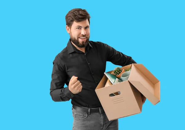 Fired young man holding box with his office stuff on blue background