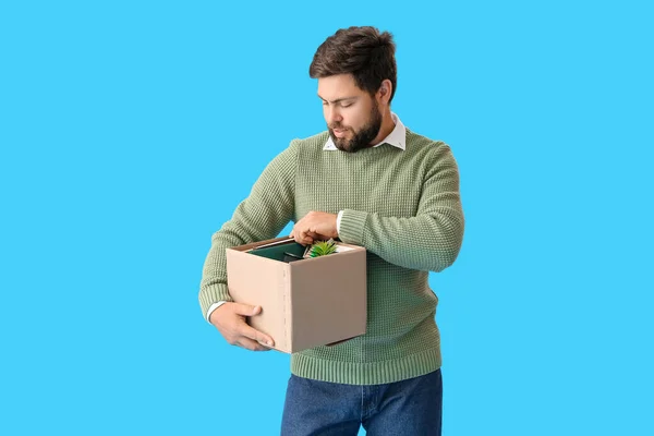 Fired young man holding box with personal stuff on blue background