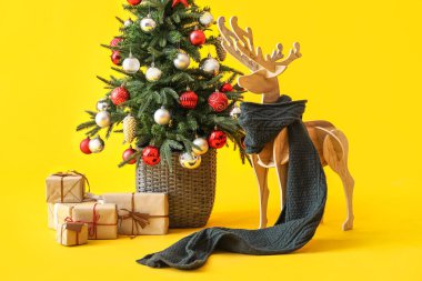 Eşarplı tahta ren geyiği, Noel ağacı ve sarı arka planda hediyeler.