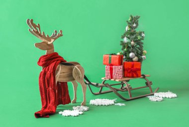 Ahşap rengeyiği eşarp, kızak, Noel ağacı ve yeşil arka planda hediyeler.