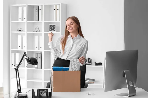 Happy fired young woman packing her personal stuff in office