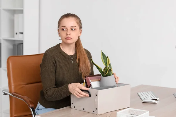 Fired young woman with packed stuff sitting at table in office