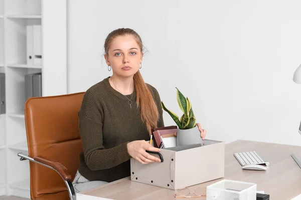 Fired young woman with packed stuff sitting at table in office