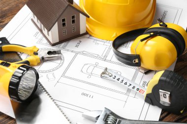 Koyu ahşap arka planda inşaat aletleri ve işitme koruyucuları olan ev planı, yakın plan