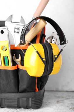 Hafif arkaplanda inşaat aletleri ve işitme koruyucuları olan çanta