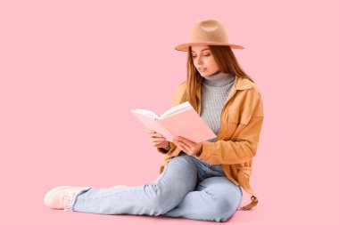 Pembe arka plan üzerine kitap okuyan genç bir kadın.