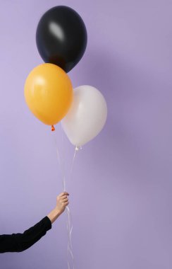 Menekşe duvarının yanında Cadılar Bayramı balonları olan kadın.