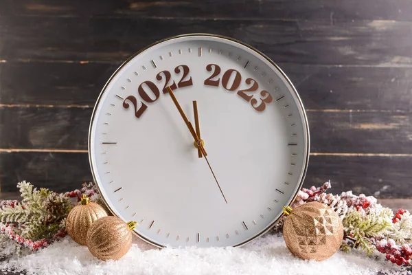 Clock with Christmas decor and snow on black wooden background. New Year time